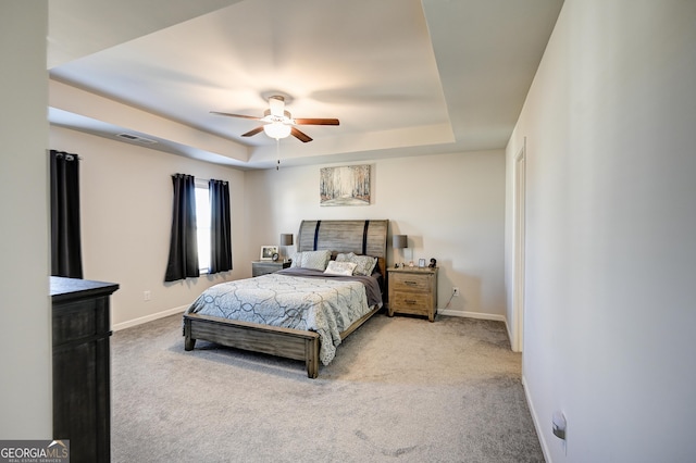 carpeted bedroom with ceiling fan and a tray ceiling