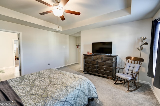 bedroom with ceiling fan, light colored carpet, and a tray ceiling