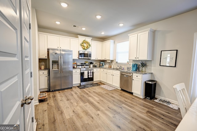 kitchen with light stone counters, white cabinets, appliances with stainless steel finishes, and sink