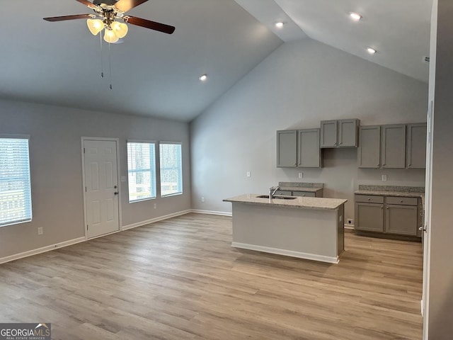 kitchen featuring sink, light hardwood / wood-style flooring, gray cabinets, light stone counters, and an island with sink