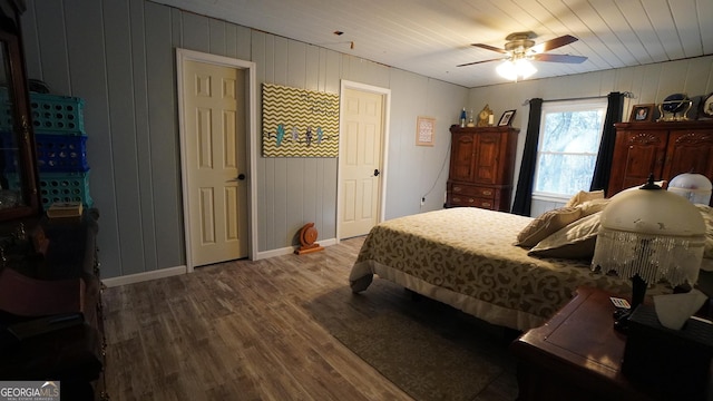 bedroom featuring ceiling fan, wood-type flooring, and wooden walls