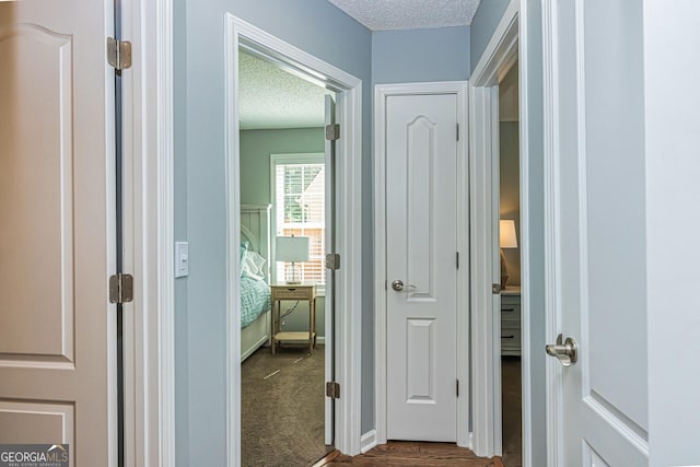 hallway featuring a textured ceiling and dark colored carpet