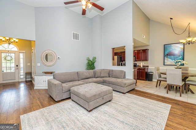 living room with ceiling fan with notable chandelier, light hardwood / wood-style flooring, and high vaulted ceiling