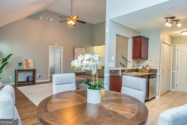 tiled dining space featuring ceiling fan, sink, a textured ceiling, and high vaulted ceiling