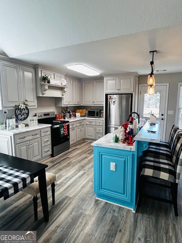 kitchen with hanging light fixtures, stainless steel appliances, hardwood / wood-style floors, and a textured ceiling