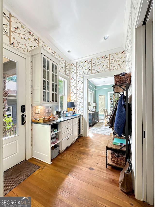 kitchen featuring light wood-type flooring, beverage cooler, crown molding, white cabinets, and sink