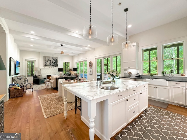 kitchen with pendant lighting, a center island with sink, sink, beamed ceiling, and white cabinets