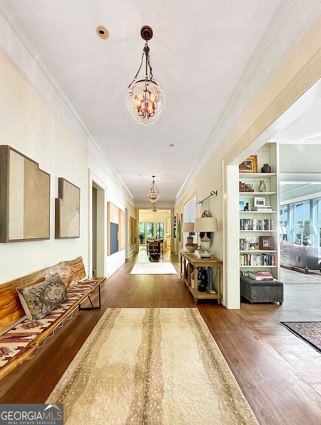 corridor featuring built in features, a notable chandelier, ornamental molding, and hardwood / wood-style floors