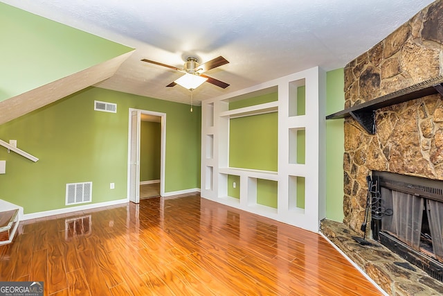 unfurnished living room with ceiling fan, a fireplace, wood-type flooring, a textured ceiling, and built in shelves