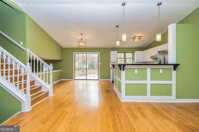 kitchen with appliances with stainless steel finishes, lofted ceiling, decorative light fixtures, white cabinetry, and light hardwood / wood-style flooring