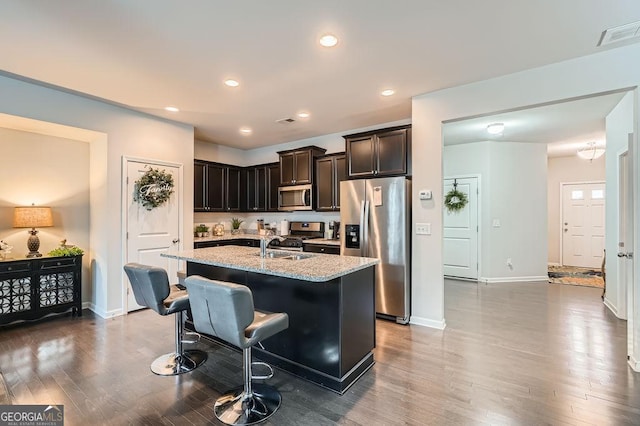 kitchen featuring dark wood-type flooring, appliances with stainless steel finishes, light stone countertops, and a kitchen island with sink