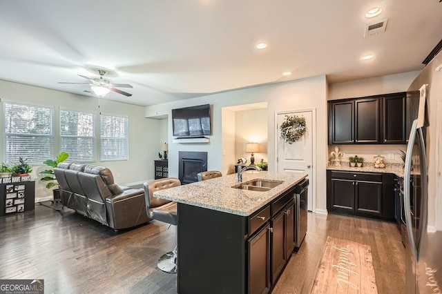 kitchen with a breakfast bar, wood-type flooring, sink, light stone counters, and a center island with sink