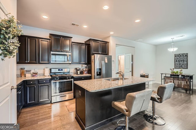 kitchen featuring pendant lighting, sink, stainless steel appliances, light stone countertops, and a center island with sink