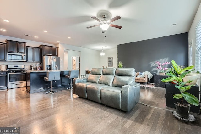 living room featuring ceiling fan with notable chandelier and light hardwood / wood-style flooring