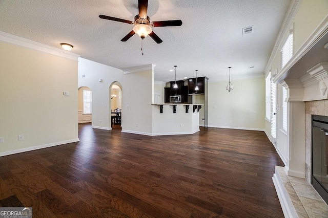 unfurnished living room featuring ceiling fan with notable chandelier, a textured ceiling, a tile fireplace, and crown molding