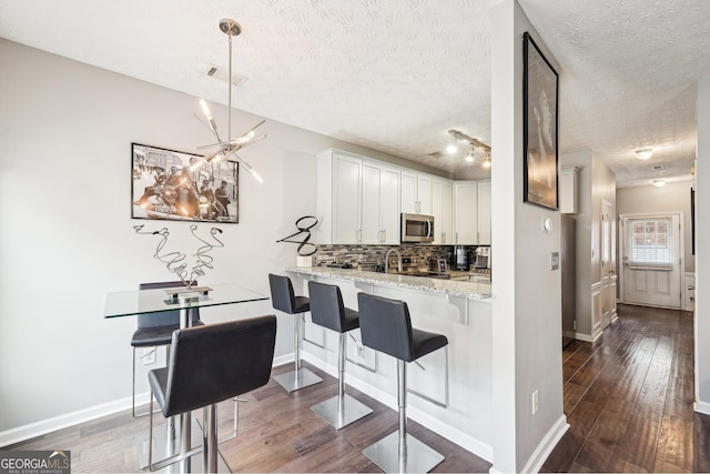 kitchen featuring white cabinets, a kitchen bar, kitchen peninsula, stainless steel appliances, and light stone countertops