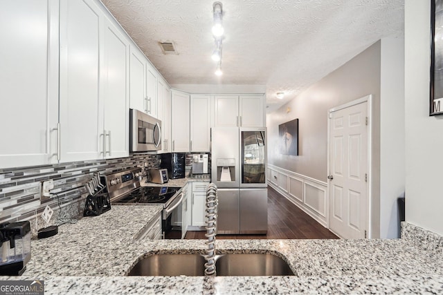 kitchen with sink, white cabinetry, a textured ceiling, stainless steel appliances, and light stone countertops