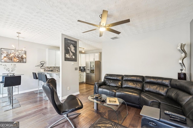 living room with ceiling fan with notable chandelier, a textured ceiling, and light wood-type flooring