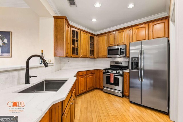 kitchen featuring a sink, light stone counters, stainless steel appliances, brown cabinetry, and crown molding