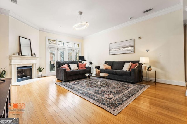 living area with visible vents, crown molding, baseboards, light wood-style floors, and a glass covered fireplace