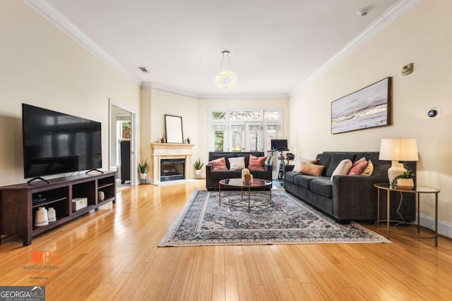 living room with a glass covered fireplace, ornamental molding, baseboards, and wood finished floors