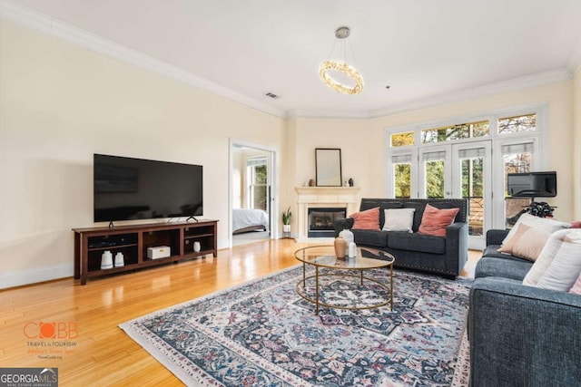 living room featuring visible vents, a glass covered fireplace, wood finished floors, crown molding, and baseboards