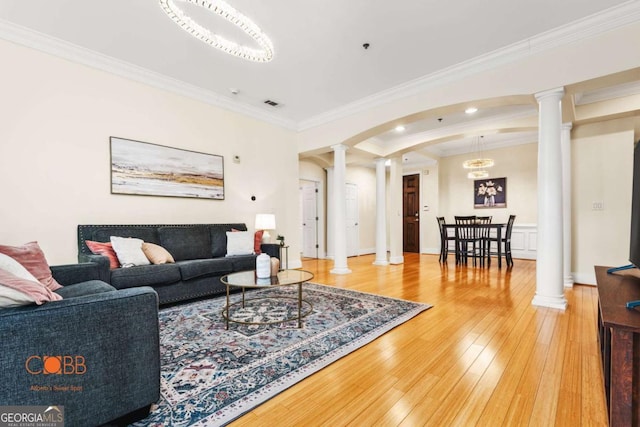 living room with hardwood / wood-style floors, crown molding, decorative columns, and arched walkways