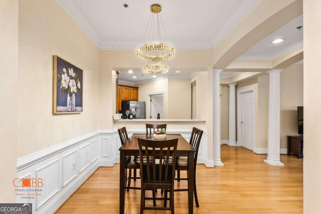 dining space featuring light wood-type flooring, a chandelier, ornamental molding, and ornate columns