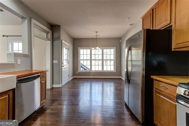 kitchen with a notable chandelier, dark hardwood / wood-style floors, hanging light fixtures, appliances with stainless steel finishes, and butcher block counters