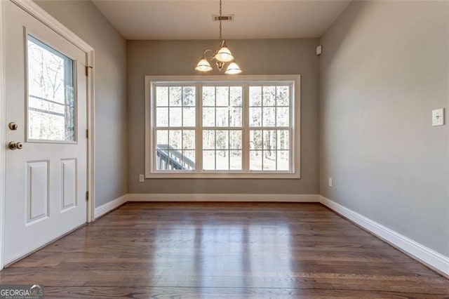 unfurnished dining area with dark wood-type flooring, a wealth of natural light, and a chandelier