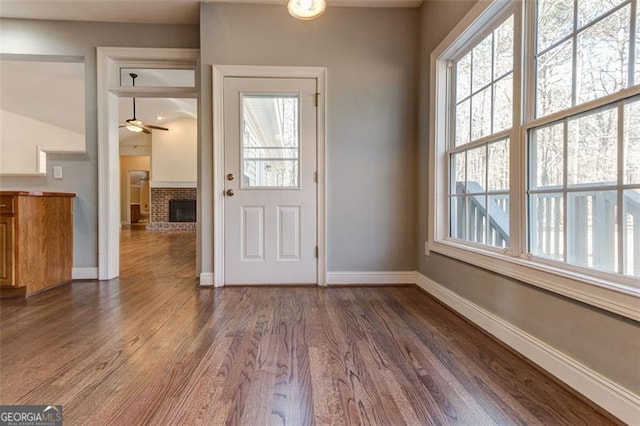 foyer entrance with ceiling fan, dark hardwood / wood-style floors, and a brick fireplace