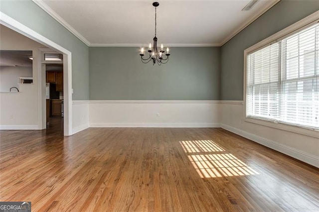 empty room featuring ornamental molding, wood-type flooring, and a notable chandelier