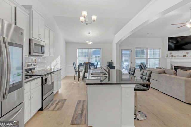 kitchen featuring a kitchen bar, stainless steel appliances, decorative light fixtures, a kitchen island with sink, and white cabinets