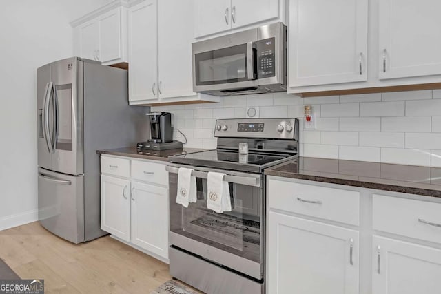 kitchen with stainless steel appliances, decorative backsplash, light wood-type flooring, dark stone counters, and white cabinets