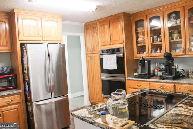 kitchen with light stone countertops, ornamental molding, stainless steel appliances, and a textured ceiling