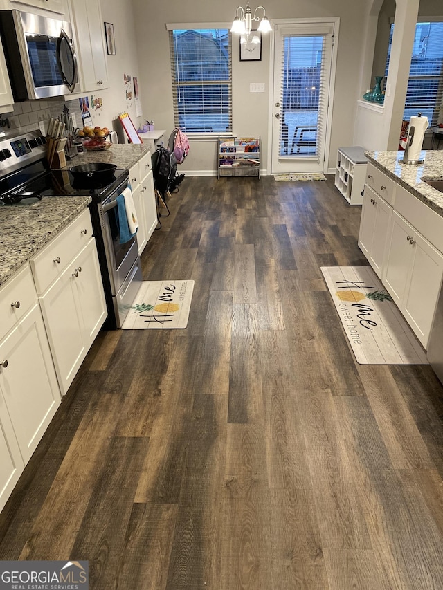 kitchen with white cabinets, dark hardwood / wood-style flooring, hanging light fixtures, light stone counters, and stainless steel appliances