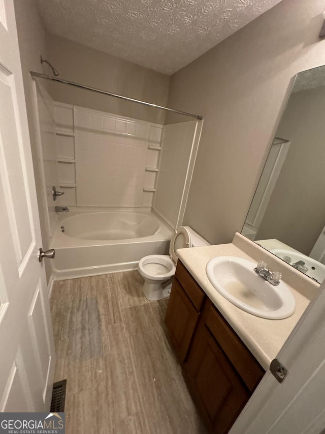 full bathroom with a textured ceiling, wood-type flooring, vanity, shower / washtub combination, and toilet