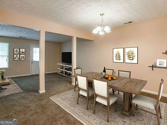 carpeted dining room featuring a chandelier and a textured ceiling