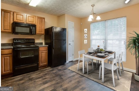 kitchen with a textured ceiling, black appliances, dark wood-type flooring, hanging light fixtures, and a notable chandelier