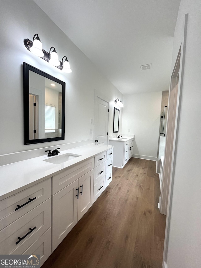 full bath with wood finished floors, walk in shower, two vanities, a sink, and visible vents