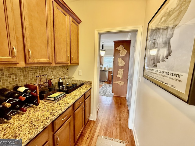 bar featuring stainless steel dishwasher, decorative backsplash, light stone counters, and light hardwood / wood-style floors