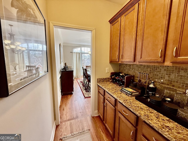 kitchen with light stone countertops, decorative backsplash, ornamental molding, light hardwood / wood-style flooring, and black electric cooktop