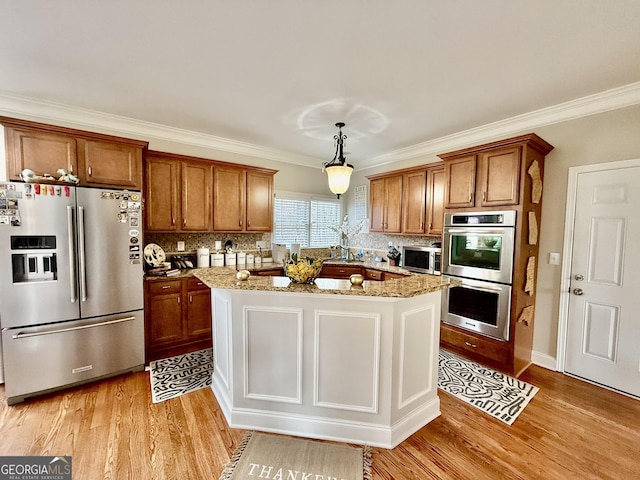 kitchen featuring stainless steel appliances, crown molding, light stone counters, and decorative light fixtures