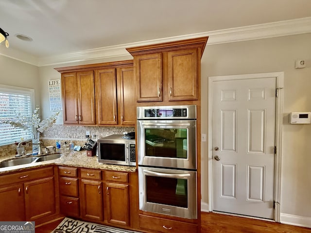 kitchen with appliances with stainless steel finishes, dark wood-type flooring, sink, backsplash, and ornamental molding