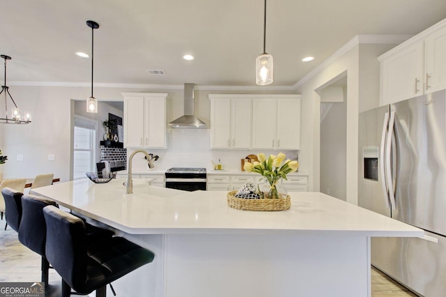 kitchen with pendant lighting, appliances with stainless steel finishes, wall chimney exhaust hood, and an island with sink