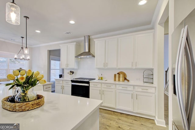 kitchen with pendant lighting, gas range oven, wall chimney exhaust hood, white cabinets, and stainless steel fridge