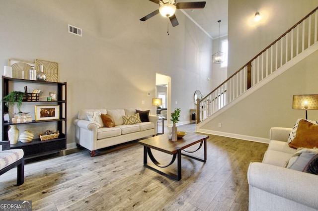 living room with ceiling fan, hardwood / wood-style floors, crown molding, and a high ceiling