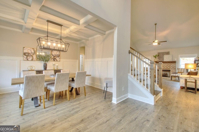 dining space featuring a fireplace, beam ceiling, coffered ceiling, hardwood / wood-style flooring, and ceiling fan with notable chandelier