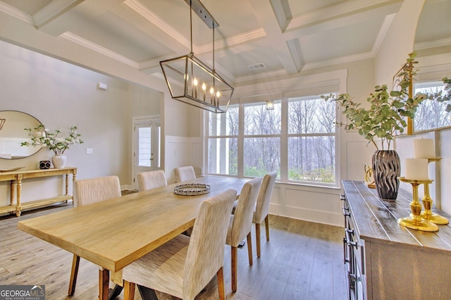 dining space with beamed ceiling, a chandelier, hardwood / wood-style flooring, crown molding, and coffered ceiling