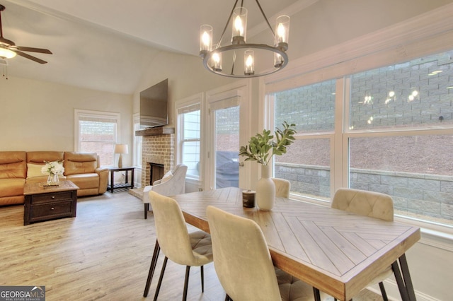 dining space with lofted ceiling, a fireplace, ceiling fan with notable chandelier, and light hardwood / wood-style flooring